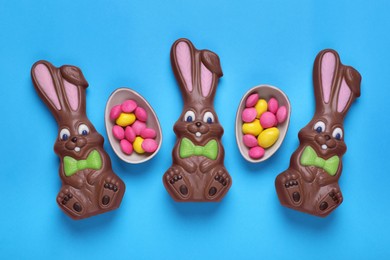 Chocolate Easter bunnies, halves of egg with candies on light blue background, flat lay