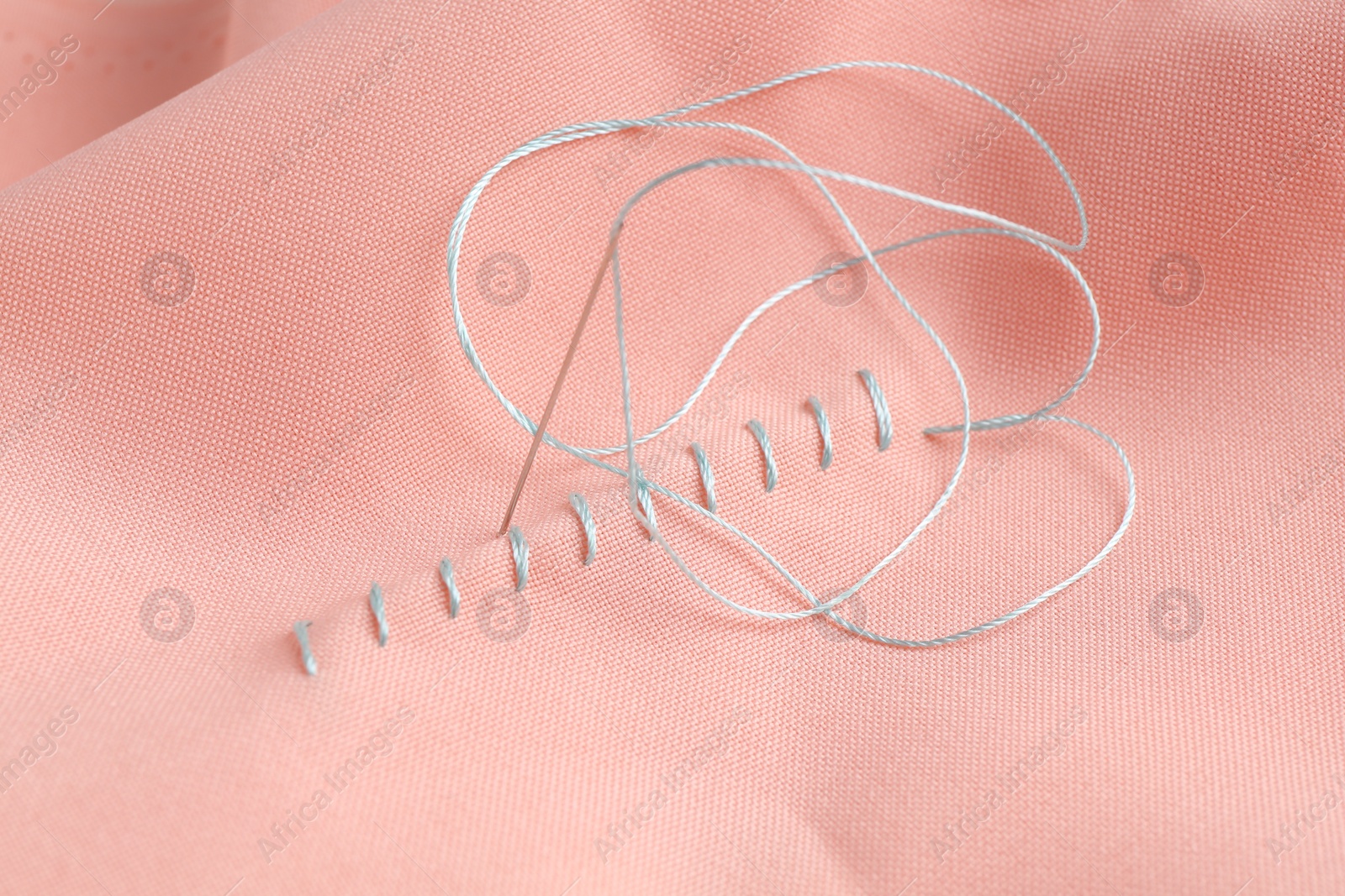 Photo of Sewing needle with thread and stitches on coral cloth, top view