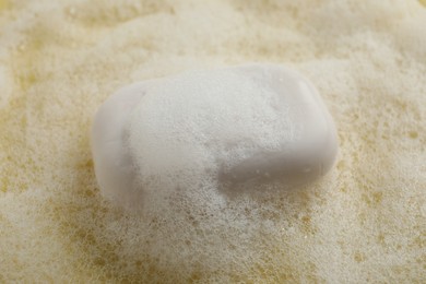 Photo of Soap with fluffy foam on yellow background, closeup