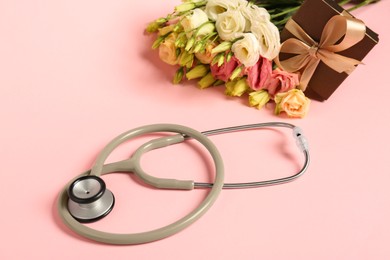 Photo of Stethoscope, gift box and eustoma flowers on pink background. Happy Doctor's Day