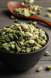 Bowl of dry cardamom pods on wooden table, closeup