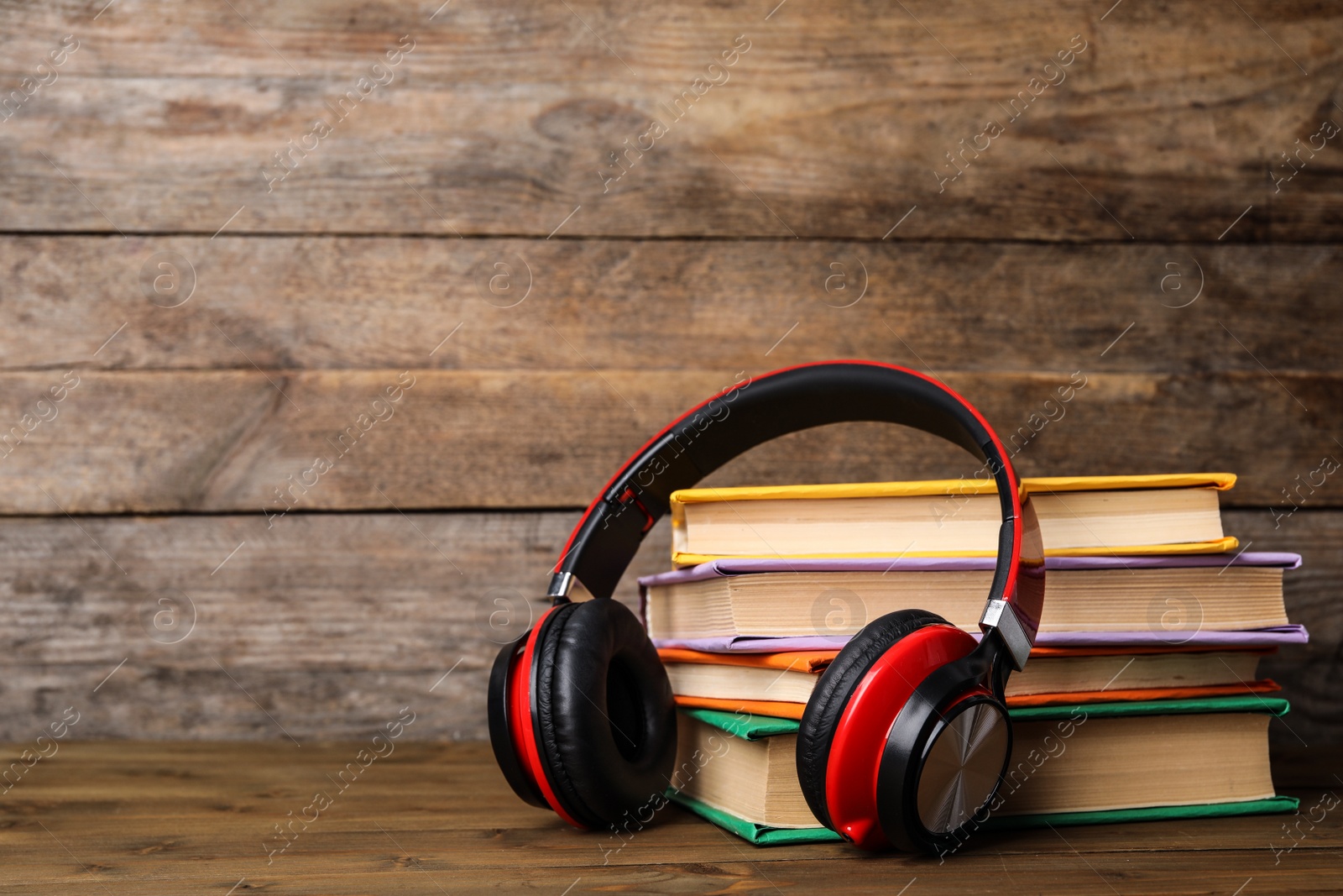 Photo of Books and modern headphones on wooden table. Space for text