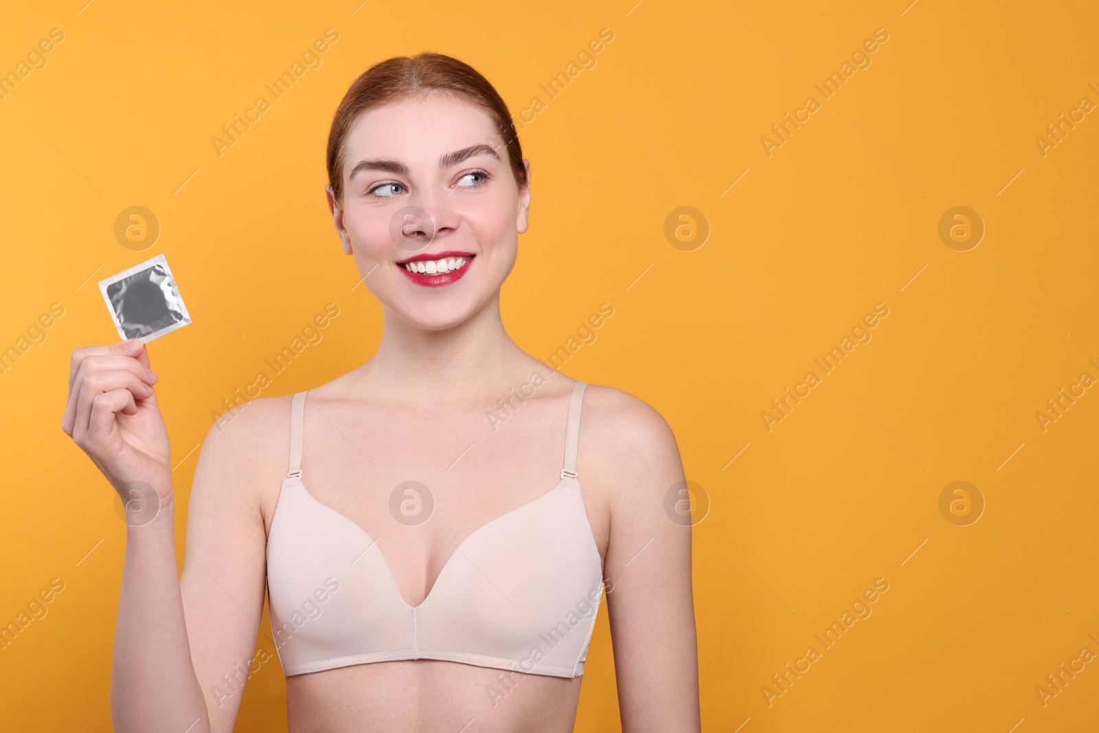 Photo of Woman in bra holding condom on yellow background, space for text. Safe sex