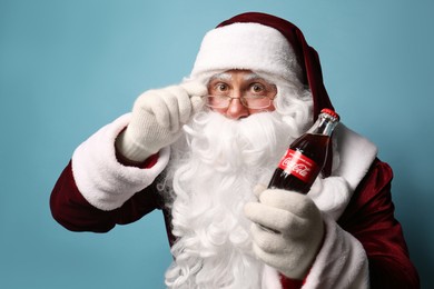 MYKOLAIV, UKRAINE - JANUARY 18, 2021: Santa Claus holding Coca-Cola bottle on light blue background