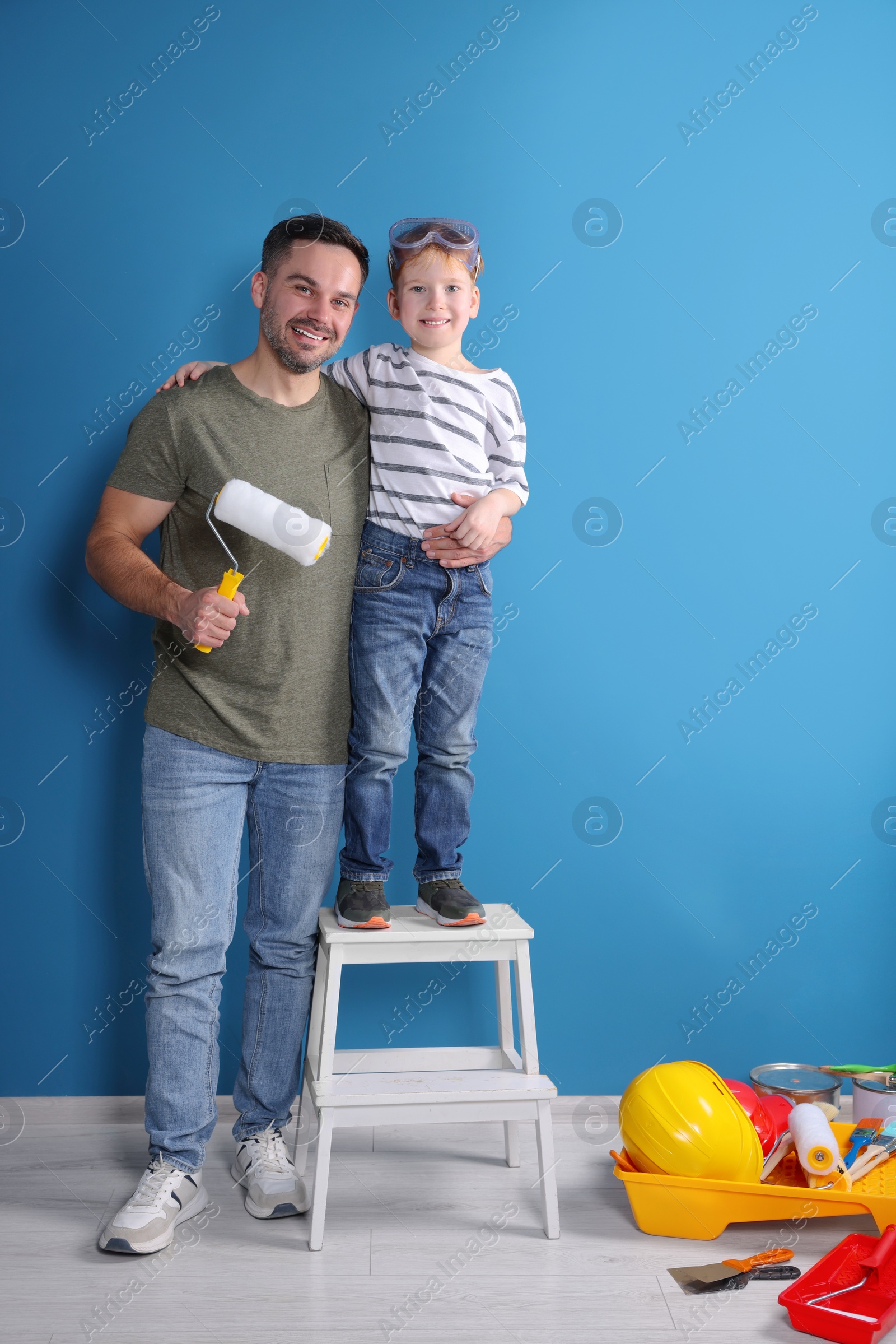 Photo of Father and son with roller near blue wall. Repair work
