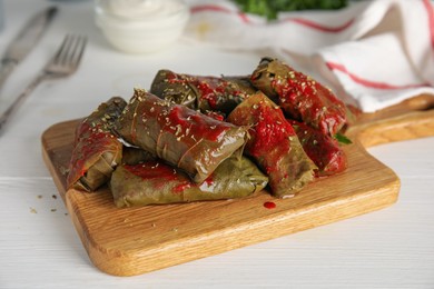 Photo of Delicious stuffed grape leaves with tomato sauce on white wooden table