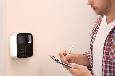 Photo of Young man checking security alarm system indoors, closeup