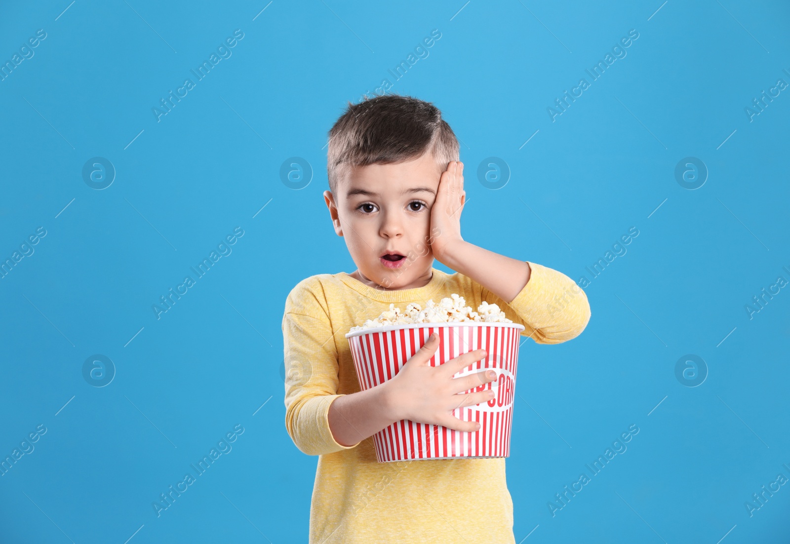 Photo of Cute little boy with popcorn on color background