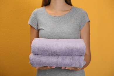 Photo of Woman holding fresh towels on orange background, closeup