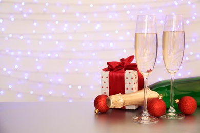 Photo of Bottle of champagne, glasses and Christmas gift on table against blurred lights