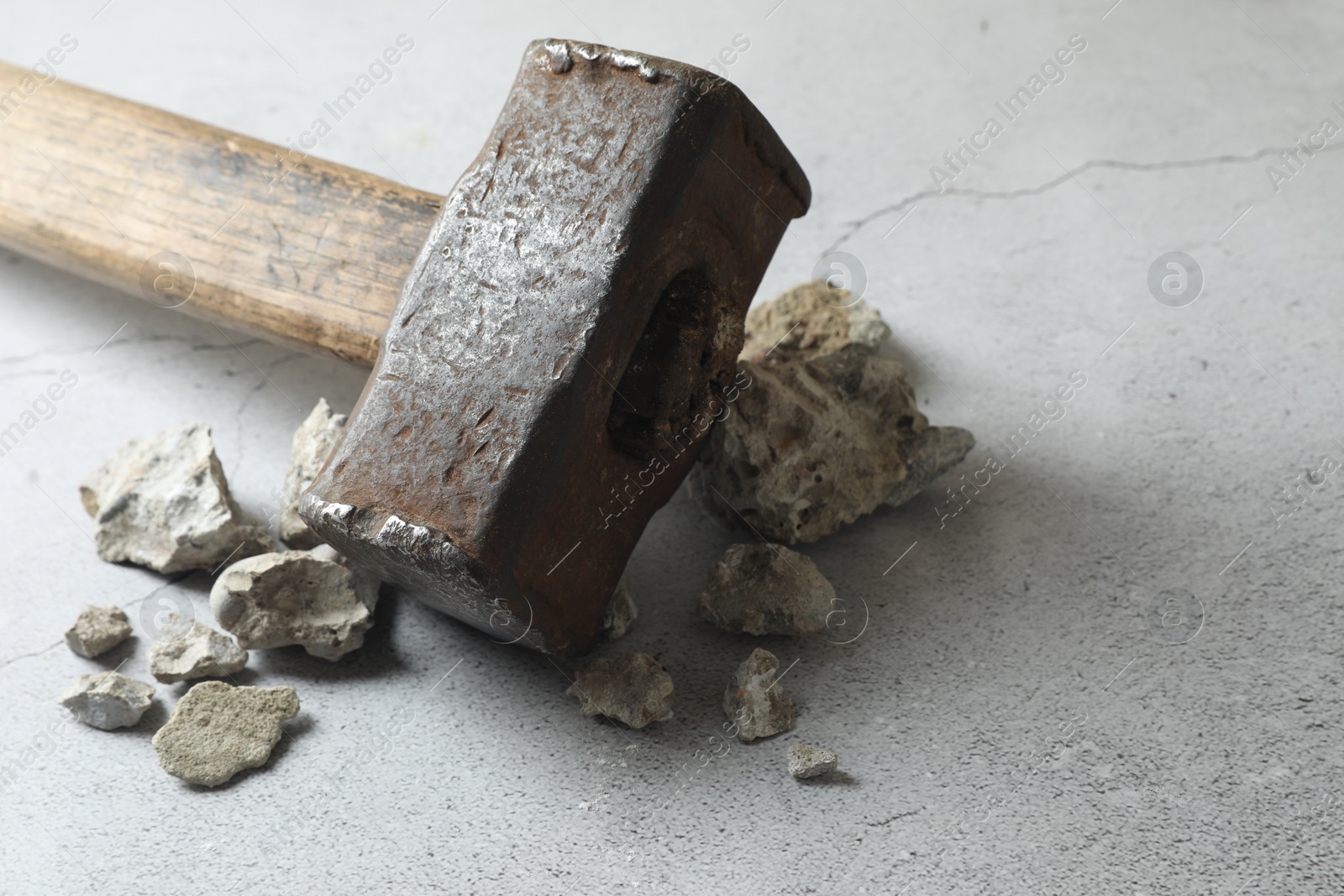 Photo of One sledgehammer and pieces of broken stones on grey textured background, closeup