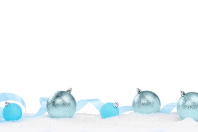 Photo of Beautiful Christmas balls and light blue ribbon on snow against white background