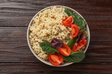 Photo of Tasty quinoa porridge with tomatoes and spinach in bowl on wooden table, top view