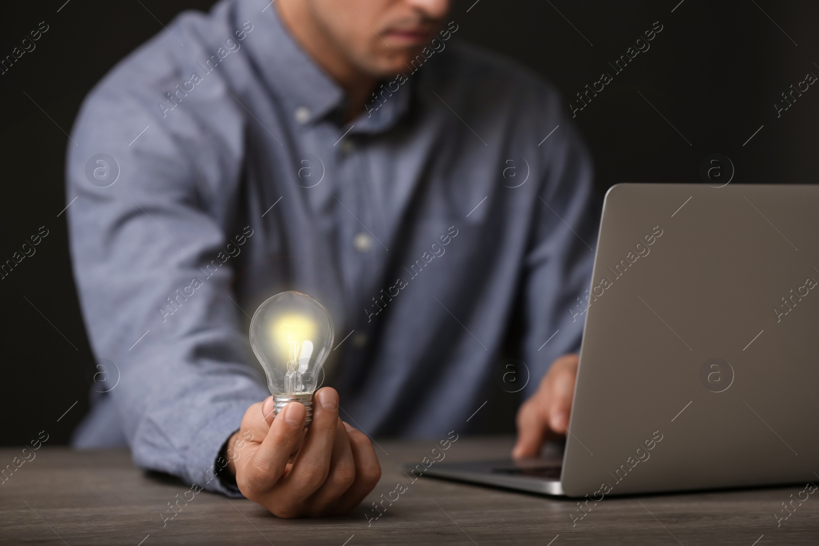 Photo of Glow up your ideas. Closeup view of man holding light bulb while working at wooden desk, space for text