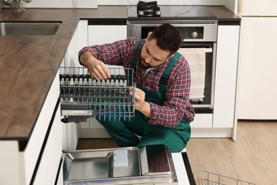 Photo of Serviceman repairing dishwasher cutlery rack in kitchen