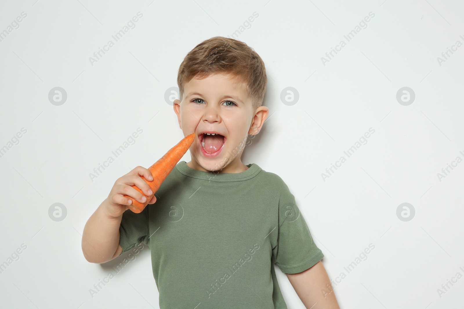 Photo of Adorable little boy eating carrot on white background. Space for text