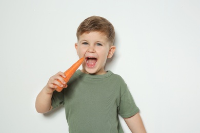 Adorable little boy eating carrot on white background. Space for text