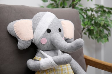Photo of Toy elephant with bandages sitting in armchair indoors