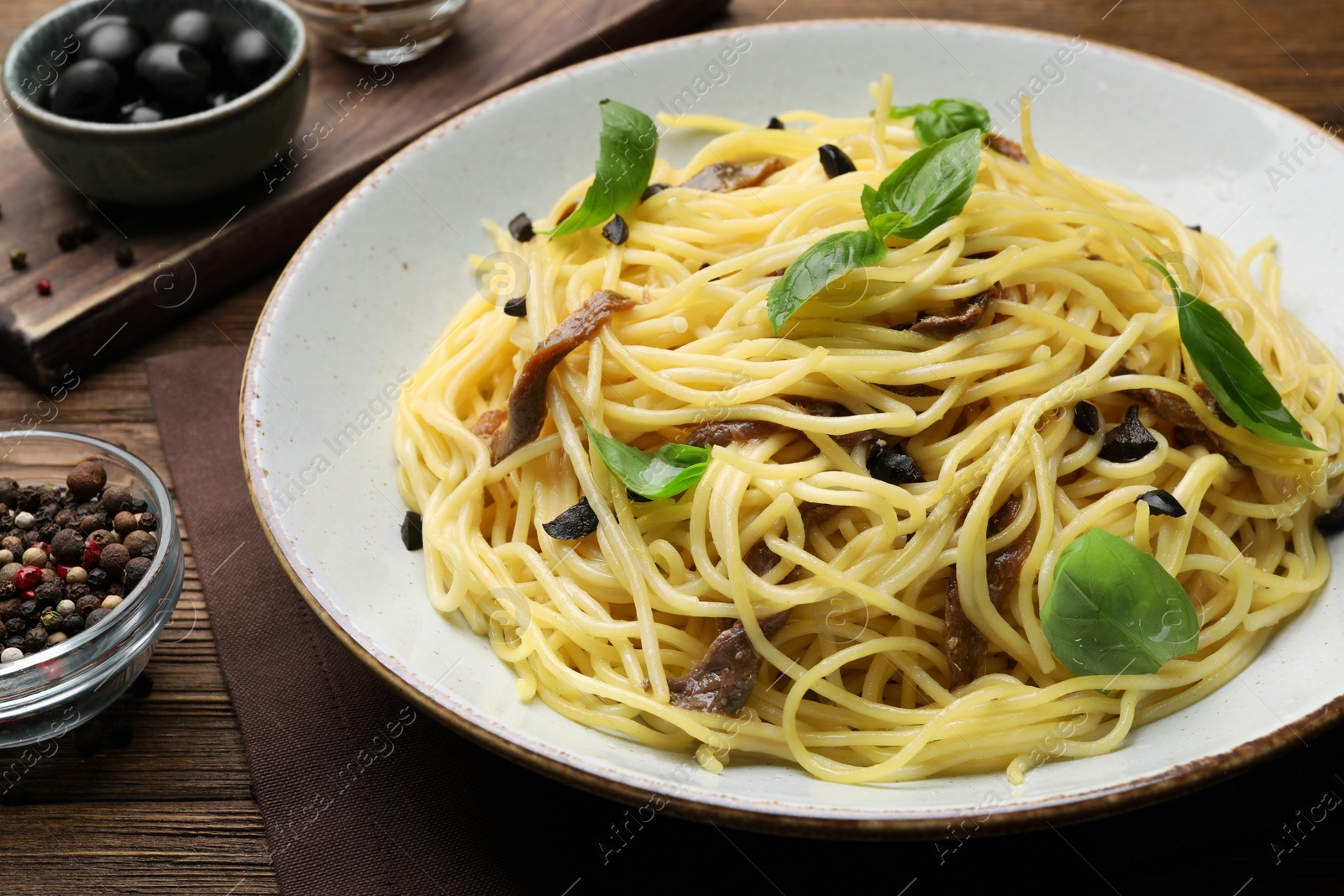 Photo of Delicious pasta with anchovies, olives and basil on wooden table, closeup