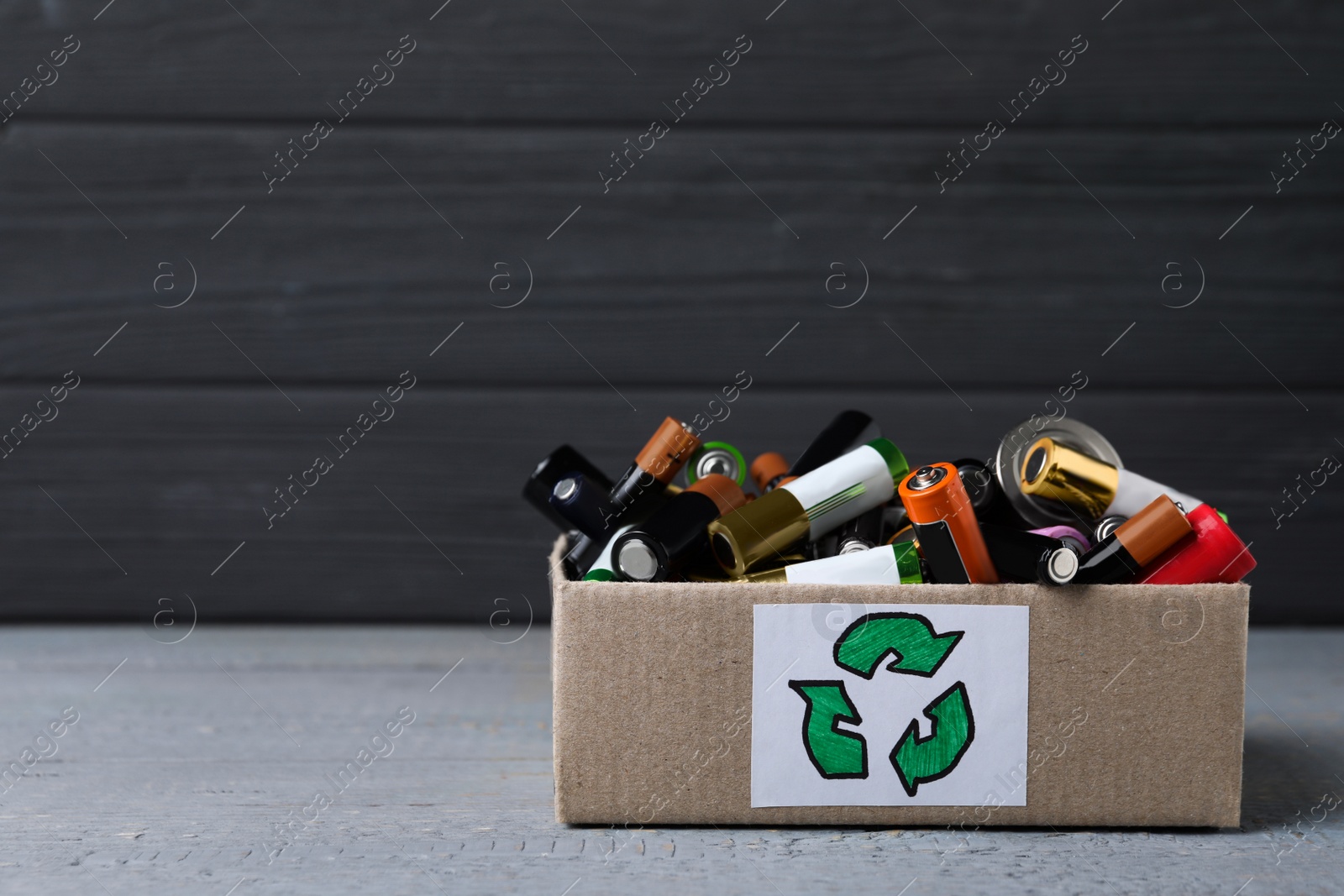 Image of Used electric batteries in cardboard box with recycling symbol on grey table. Space for text