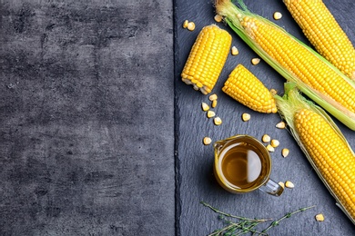 Flat lay composition with jug of corn oil and fresh cobs on dark background