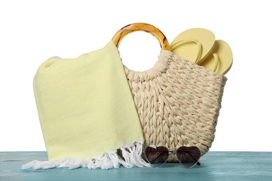 Photo of Beach bag with towel, flip flops and heart shaped sunglasses on light blue wooden surface against white background
