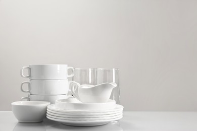 Photo of Set of many clean dishware and glasses on light table. Space for text
