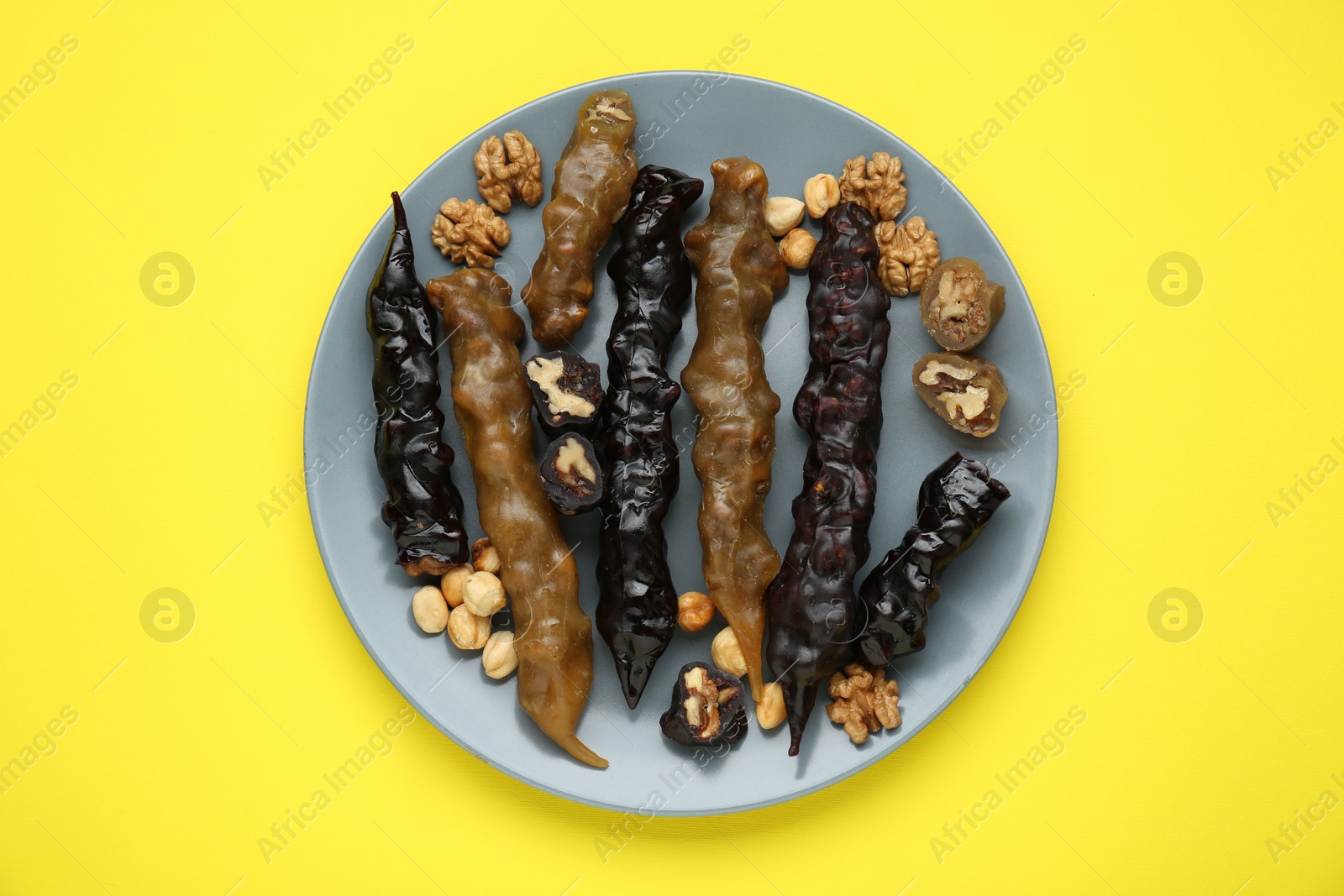 Photo of Plate with delicious churchkhelas and nuts on yellow background, top view