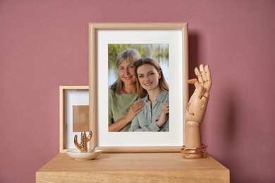 Family portrait of mother and daughter in photo frame on table near color wall