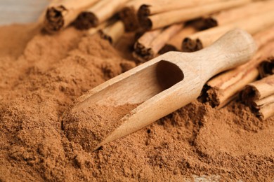 Photo of Aromatic cinnamon powder, scoop and sticks on table, closeup