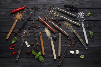 Flat lay composition with various spices, test tubes and fresh herbs on black wooden background