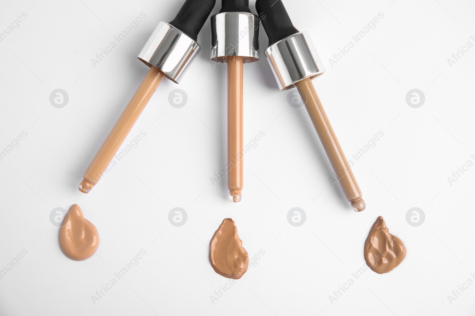 Photo of Samples of different foundation shades and droppers on white background, top view