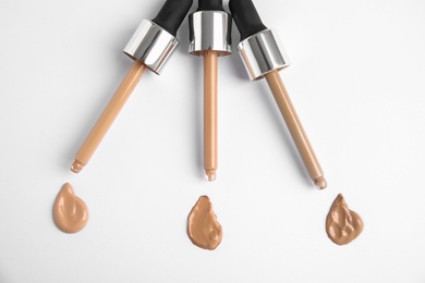 Samples of different foundation shades and droppers on white background, top view