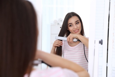 Happy woman using hair iron in front of mirror