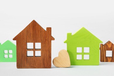 Long-distance relationship concept. Wooden heart between house models on light blue background