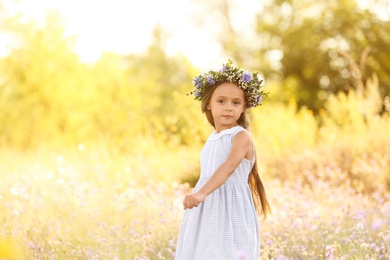 Photo of Cute little girl wearing flower wreath outdoors, space for text. Child spending time in nature