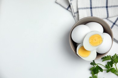 Photo of Bowl with hard boiled eggs, parsley and kitchen towel on white table, flat lay. Space for text