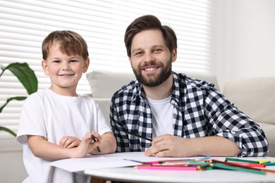 Family portrait of happy dad and son at table indoors