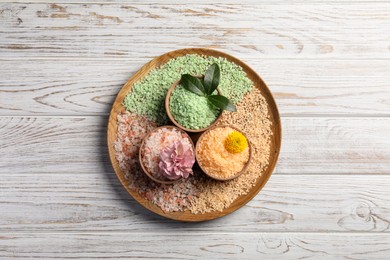 Different types of aromatic sea salt on white wooden table, top view