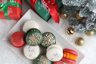 Beautifully decorated Christmas macarons, gift boxes and festive decor on snow, flat lay