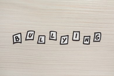Word Bullying made with paper letters on white wooden table, flat lay