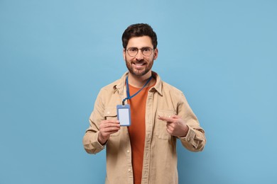 Photo of Smiling man showing VIP pass badge on light blue background