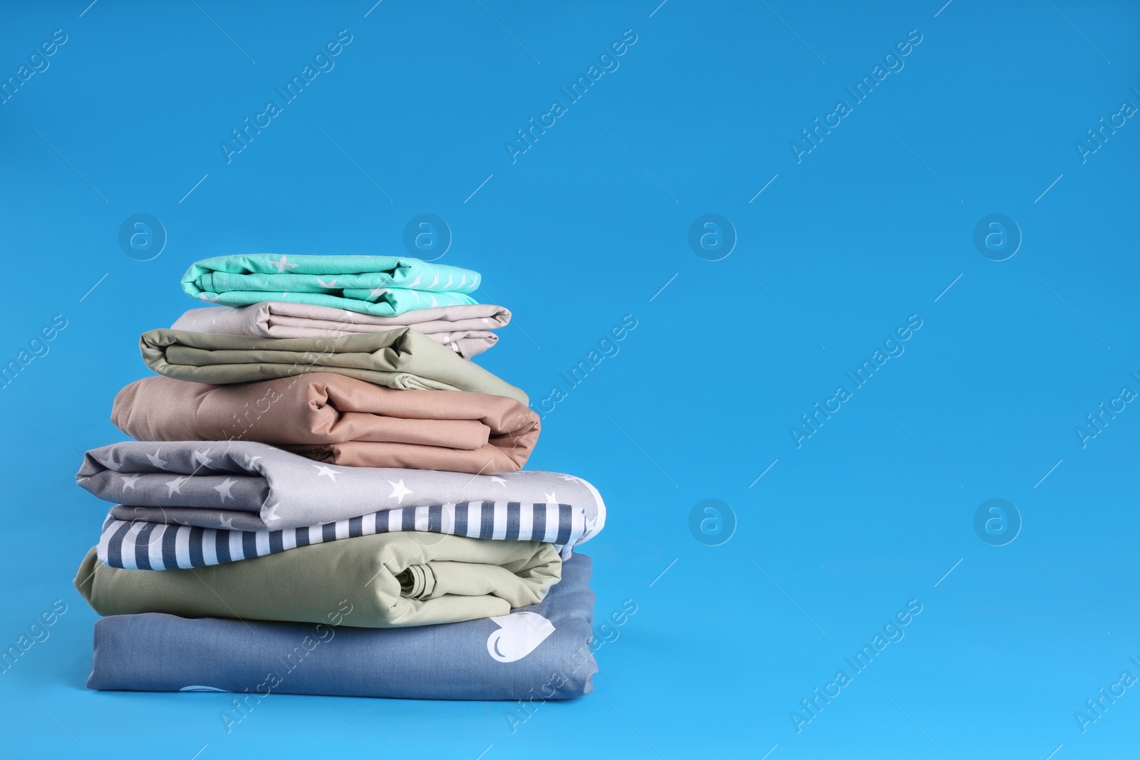 Photo of Stack of clean bed sheets on blue background. Space for text