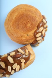 Photo of Supreme croissants with chocolate paste and nuts on light blue background, top view. Tasty puff pastry