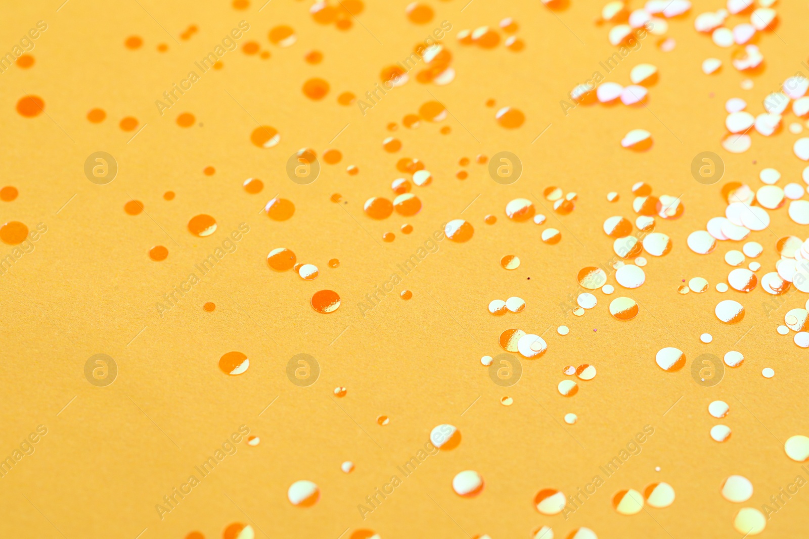 Photo of Shiny bright orange glitter on yellow background