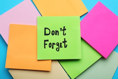 Photo of Paper with phrase Don' t Forget and many empty notes on blue background, flat lay