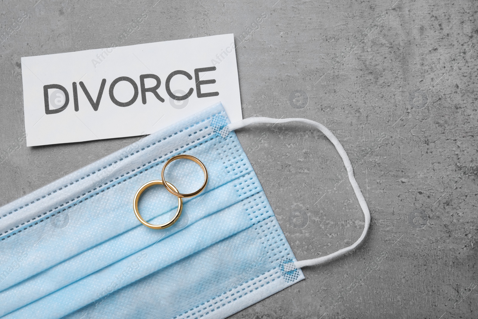 Photo of Flat lay composition with protective mask and wedding rings on grey table. Divorce during coronavirus quarantine