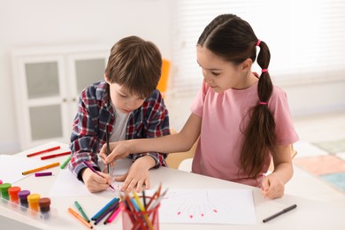 Photo of Happy brother and sister drawing at white table in room