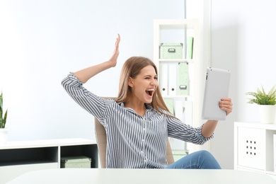 Emotional young woman with tablet celebrating victory in office