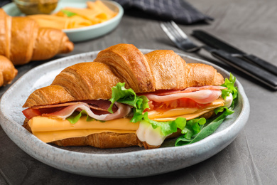 Photo of Tasty croissant sandwich with ham and cheese on grey table, closeup